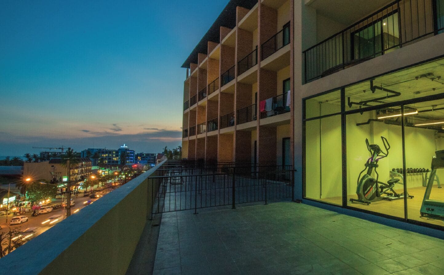 Un edificio moderno con varios balcones, amplias ventanas y vista a una ciudad al atardecer.