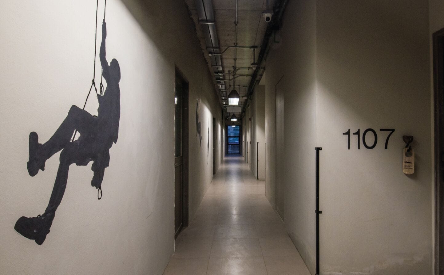 A hallway with a number sign '1107' on the wall, a silhouette of a person climbing on the left, and a door at the end.