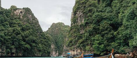 A boat on a turquoise sea with dense green cliffs in the background.
