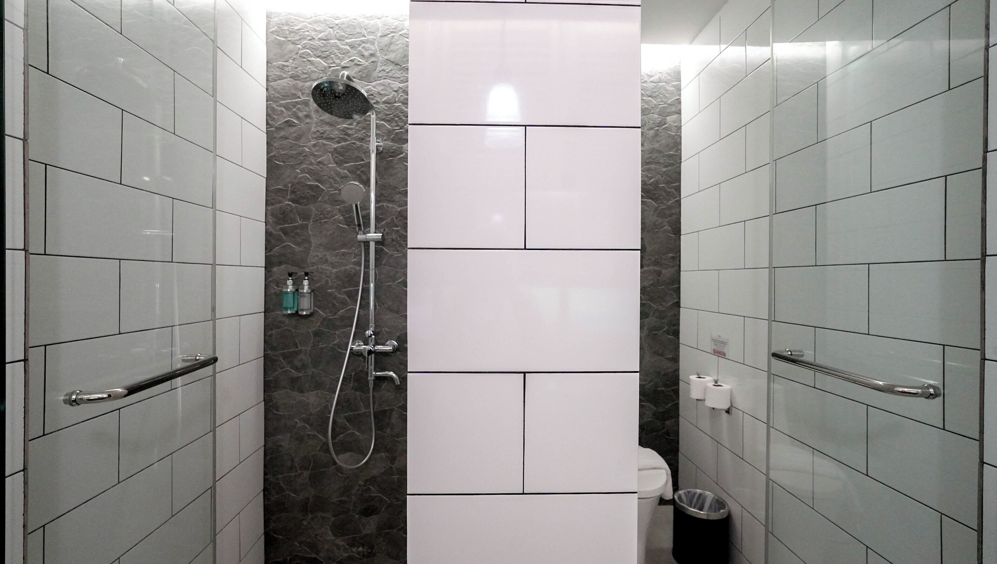 A modern bathroom with white tiles, a shower with a handheld showerhead, and a toilet.