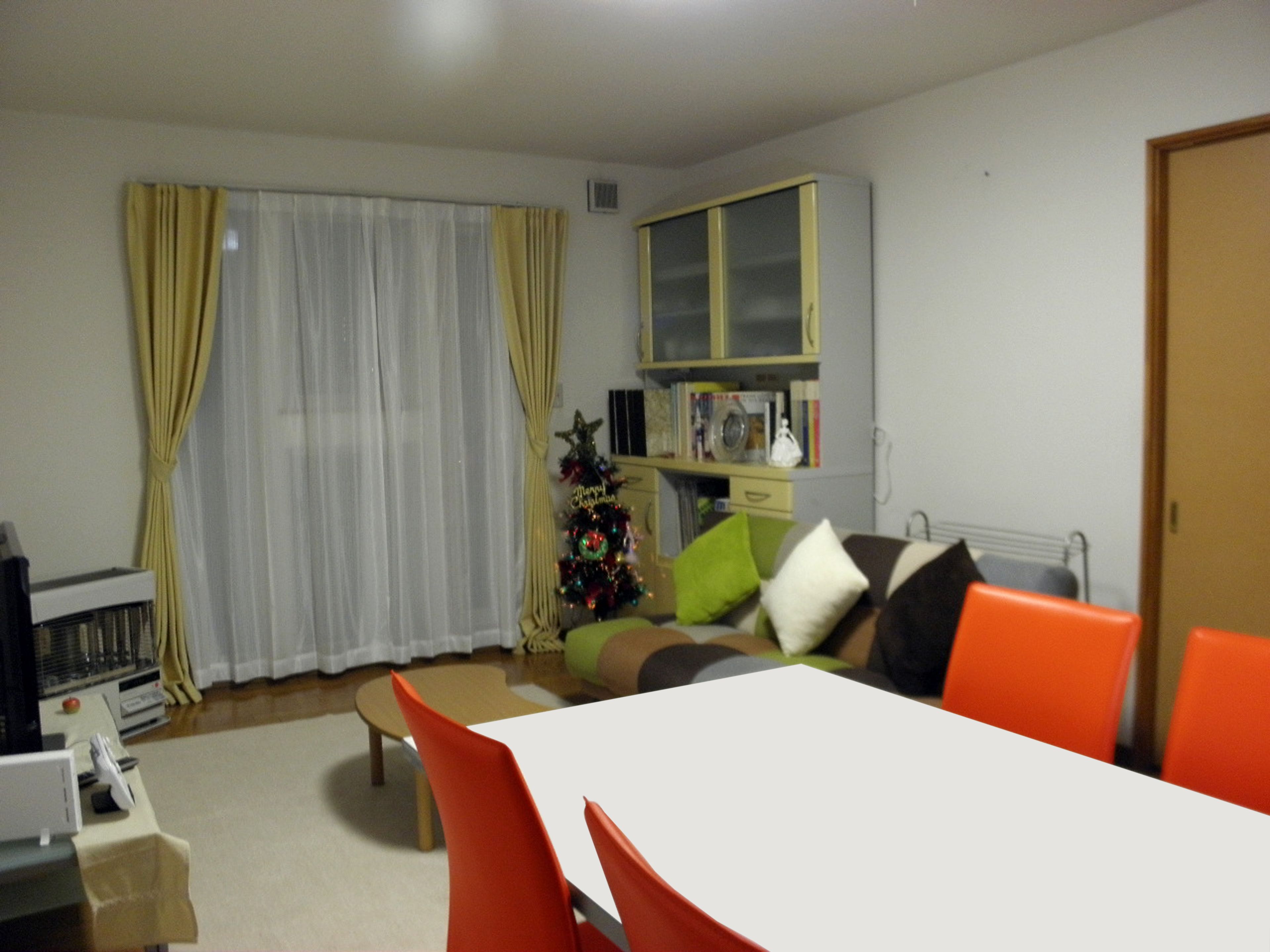 A living room with a white table, orange chairs, a Christmas tree, and a bookshelf.