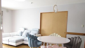 A modern living room with a sectional sofa, a round table, and two chairs. - Guesthouse Annabel (Hakodate)