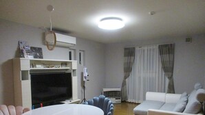 A living room with a flat-screen TV, a white sofa, a blue armchair, and a round table. - Guesthouse Annabel (Hakodate)