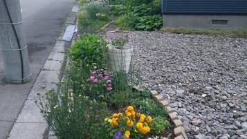 Un jardín residencial con diversas flores y plantas, un camino de grava y una valla de madera.