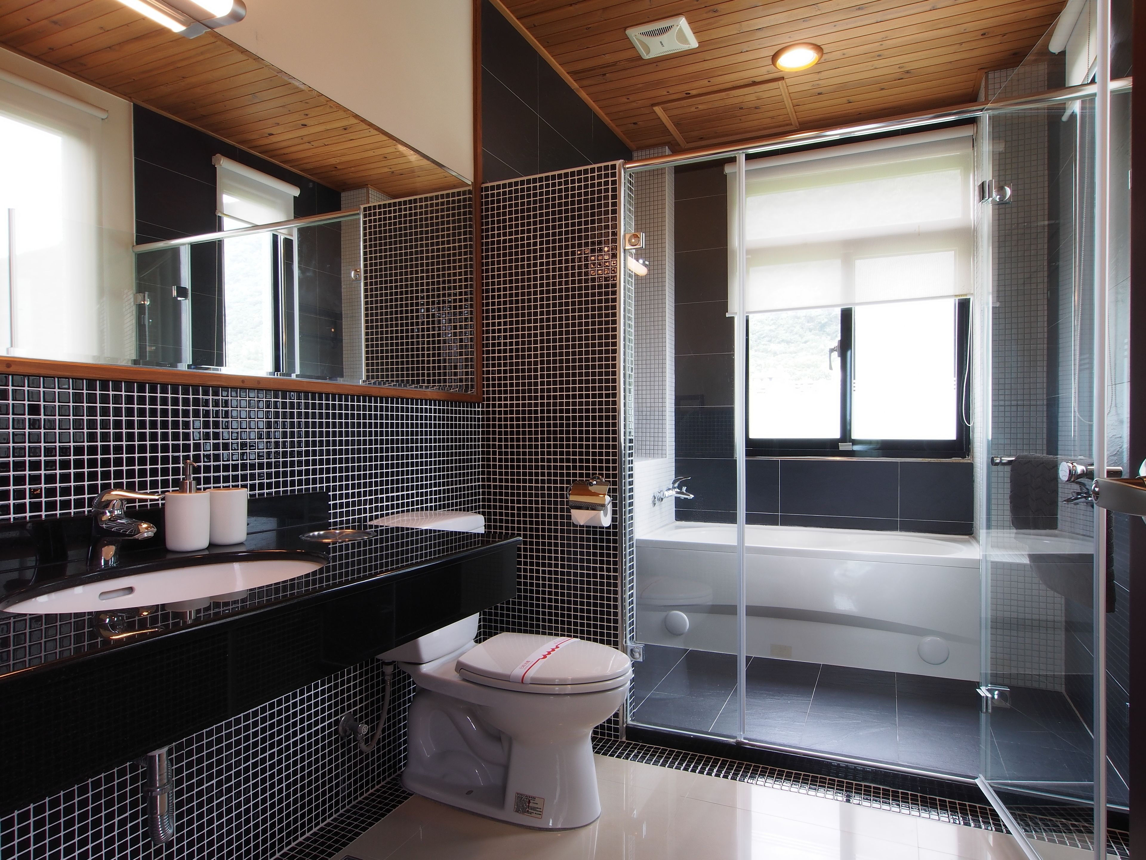 Uma casa de banho moderna com painel de azulejos preto e branco, cabine de duche em vidro e sanita branca.