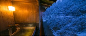 A wooden interior with a wooden bench and a small table, a wooden wall with a light fixture, and a view of a snow-covered landscape outside. - Sake Hotel Tamakiya (Tokamachi)