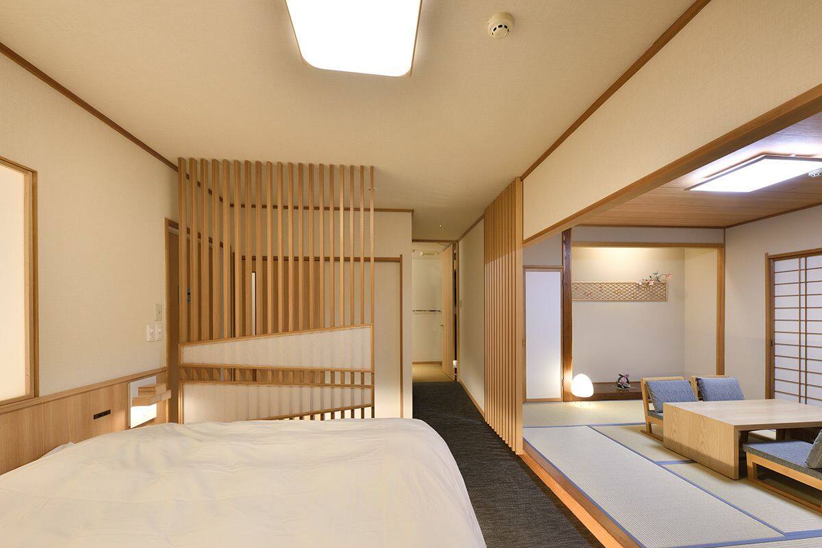 A traditional Japanese-style hotel room with tatami flooring, a low wooden bed, a small table, and a sliding door.