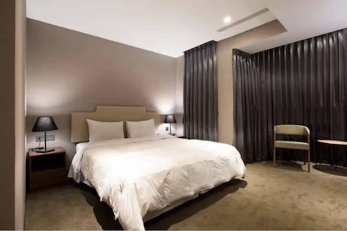 A hotel room with a bed, bedside lamps, a chair, and a small table.