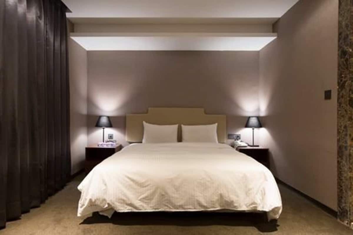 A hotel room with a large bed, two bedside tables with lamps, and a dark curtain on one side.