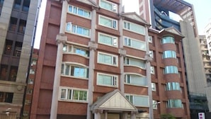 Et hotel med flere etager, en central indgang, en parkeringsplads med biler og en moderne bygning ved siden af.
