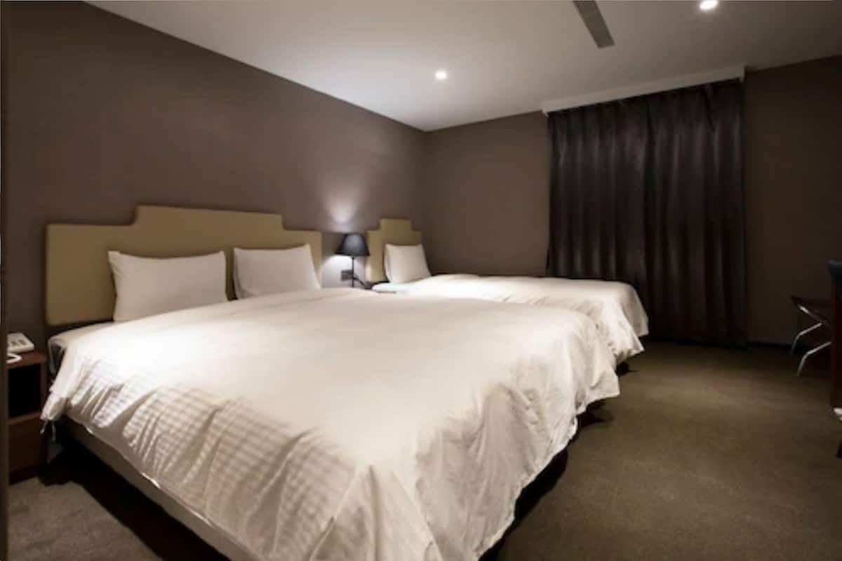 A hotel room with a large bed, two bedside tables, a lamp, and a curtain.