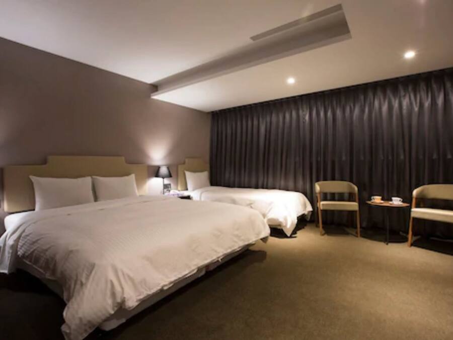 Een hotelkamer met twee bedden, een groot raam met gordijnen, een klein tafeltje en twee stoelen.