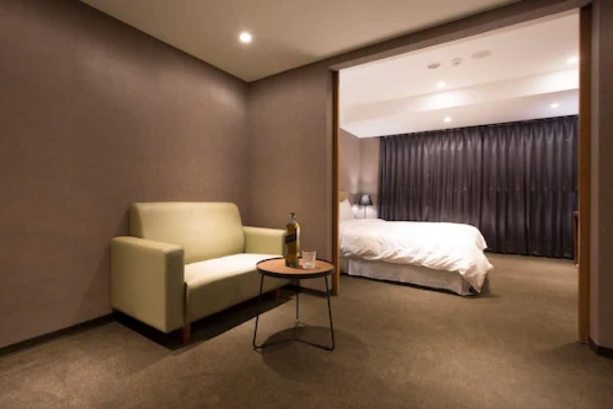 A hotel room with a single bed, a sofa, and a small table with a bottle and glass.