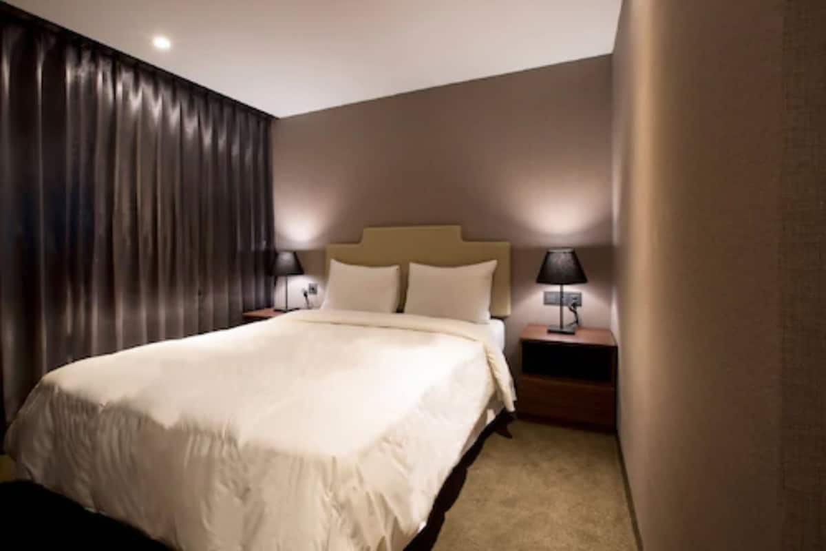 A hotel room with a large bed, two bedside tables with lamps, and a dark curtain on one wall.