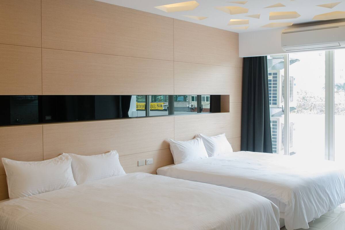 A hotel room with two beds, a large window, and a modern ceiling design.