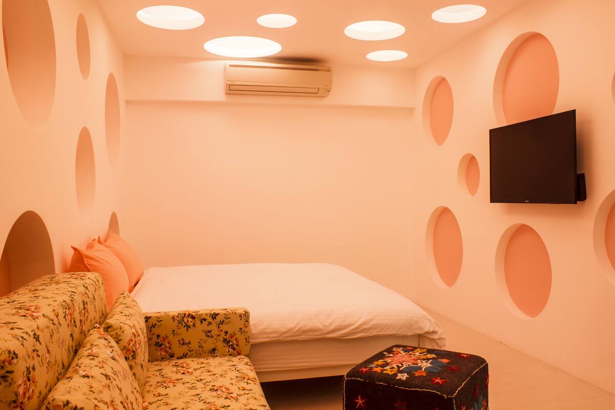 A bedroom with a bed, a sofa, a TV, and an air conditioning unit.
