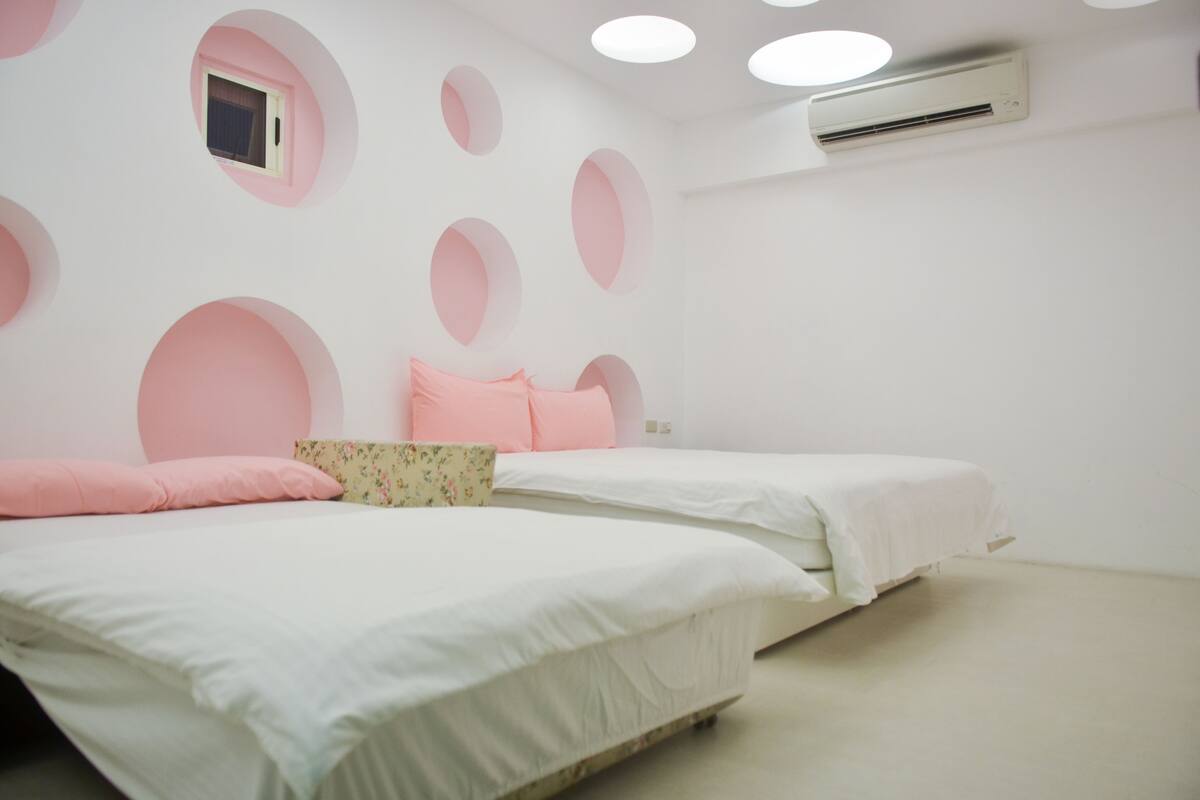 A bedroom with two beds, each with white bedding and pink pillows. There are circular wall decorations and a small window above one bed.