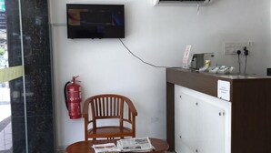 A reception area with a wooden chair, a television mounted on the wall, and a white air conditioning unit. - Hotel Al Abraar (Malacca City)