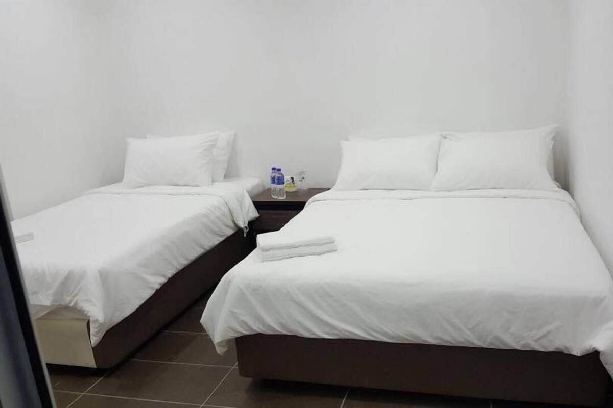 A hotel room with two single beds, a small table with a water bottle, and a nightstand.