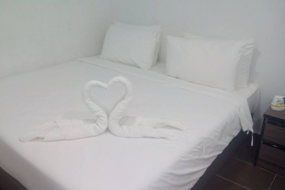 A neatly made bed with white linens and two towels arranged in a heart shape on the bed.
