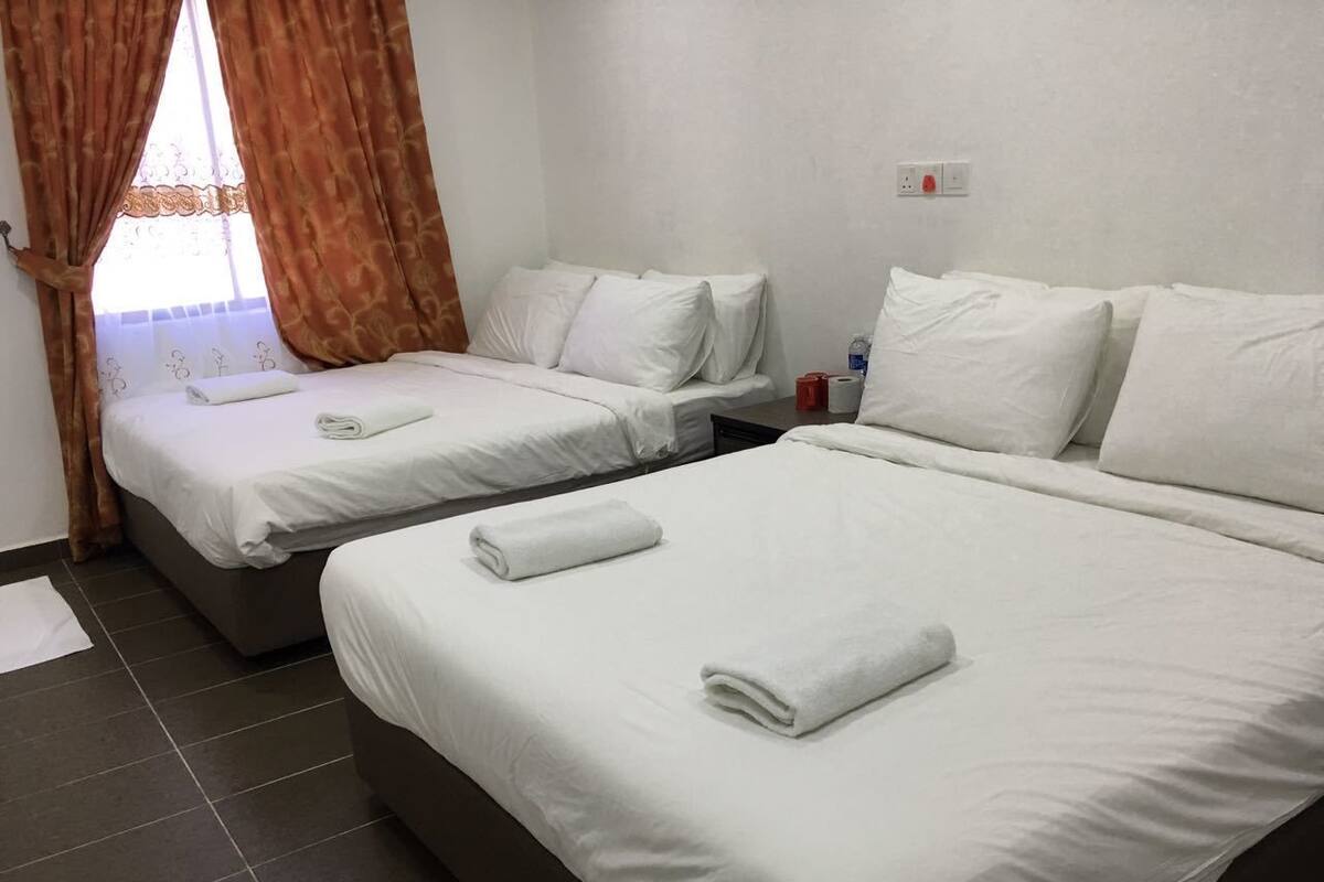 A hotel room with two single beds, each with white linens and towels, a small table with a bottle and tissues, and a window with curtains.