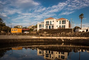 A waterfront property with a modern two-story house, a small yellow building, and a reflection in the water.