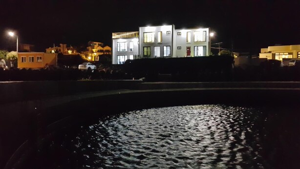 A modern building with multiple floors and large windows, situated next to a body of water. - Jeju Amoje (Seogwipo)