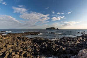 A rocky shoreline with a distant island and a clear sky.