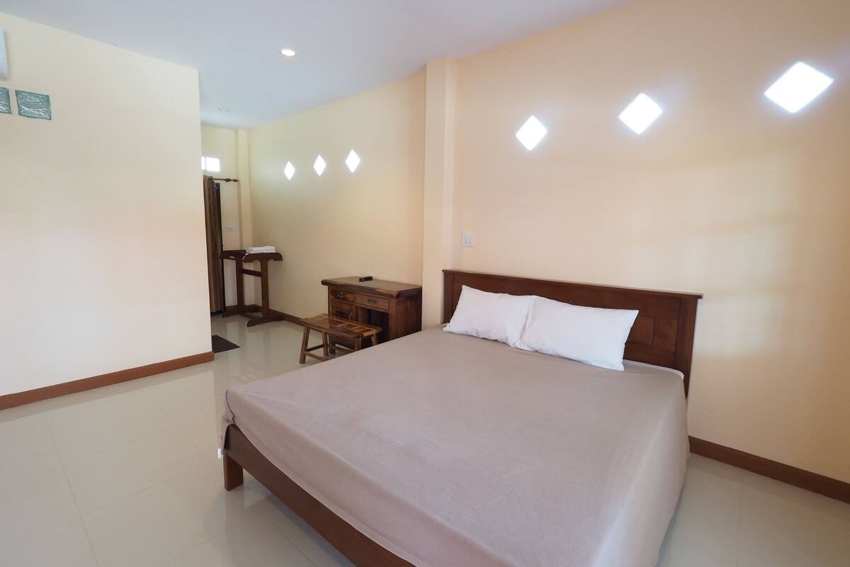 A hotel room with a large bed, a wooden nightstand, a desk, and a chair.