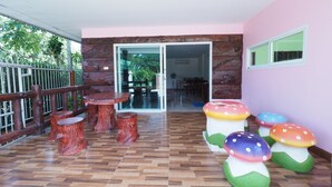 A covered patio with wooden tables and chairs, a glass door leading inside, and colorful mushroom sculptures. - Banyang Resort (Kanchanaburi)