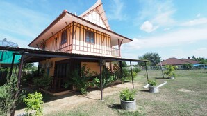 A two-story house with a sloped roof, a covered porch, and a fenced yard with potted plants. - Banyang Resort (Kanchanaburi)