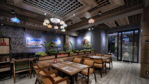 A restaurant interior with wooden tables and chairs, hanging decorative lights, and potted plants. - Sayyoh Hotel (Tashkent)