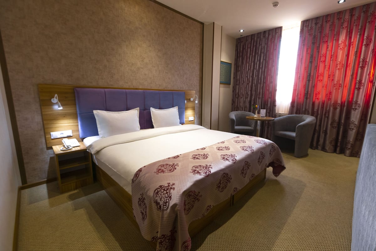 A hotel room with a large bed, a nightstand, a desk, and a chair.