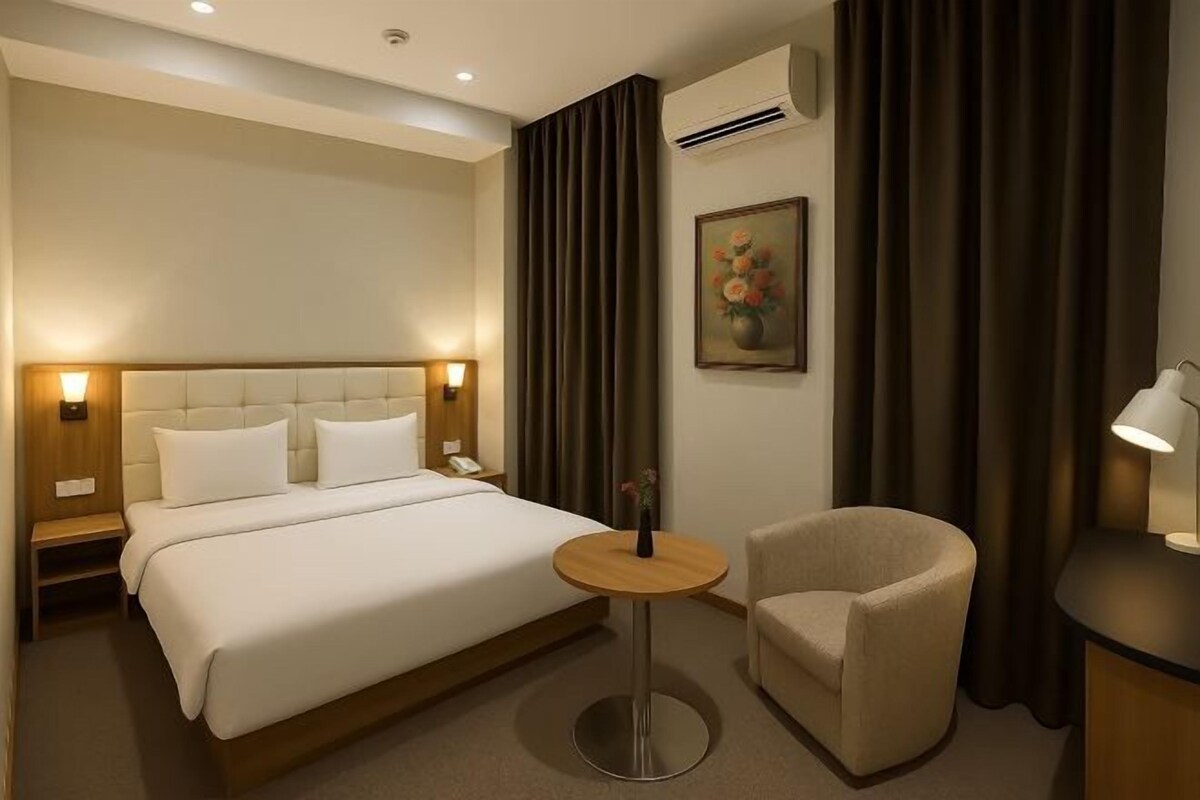 A hotel room with a large bed, a round table, a chair, and a painting on the wall.