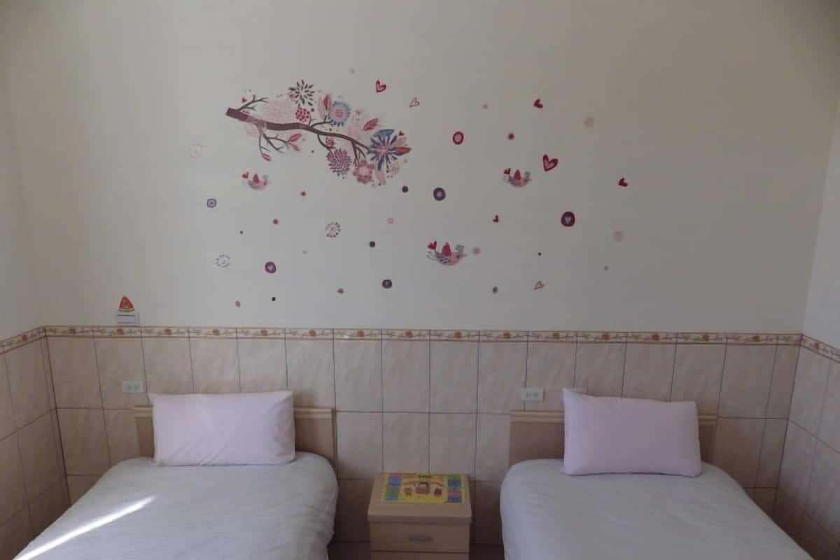 A room with two beds, each with a pillow and a nightstand with a book.