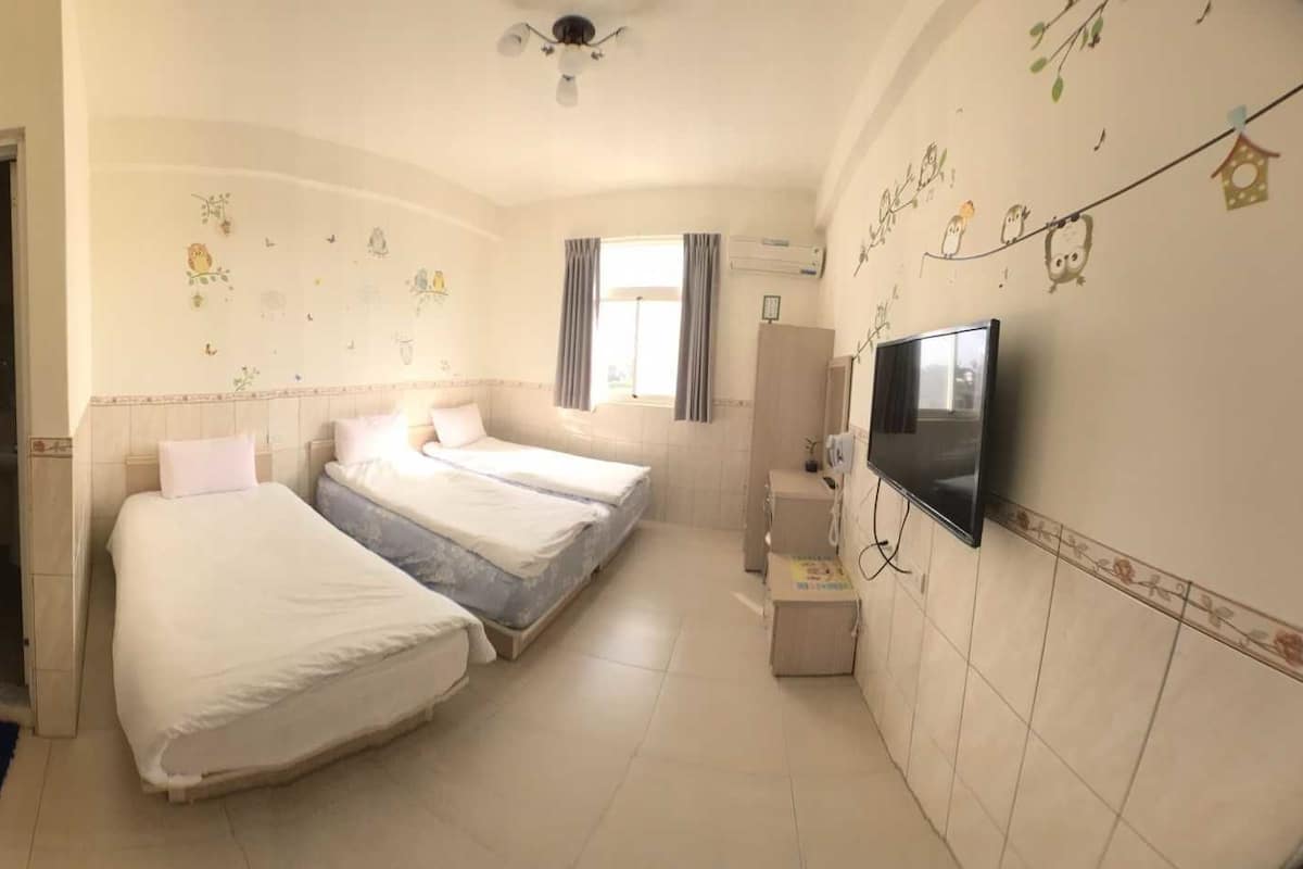 A hotel room with two beds, a TV, a small desk, and a bathroom with a toilet and sink.