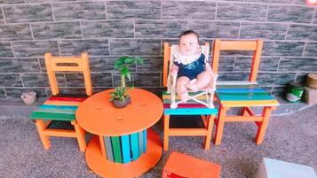 A child seated at a colorful outdoor table and chairs with a potted plant on the table.