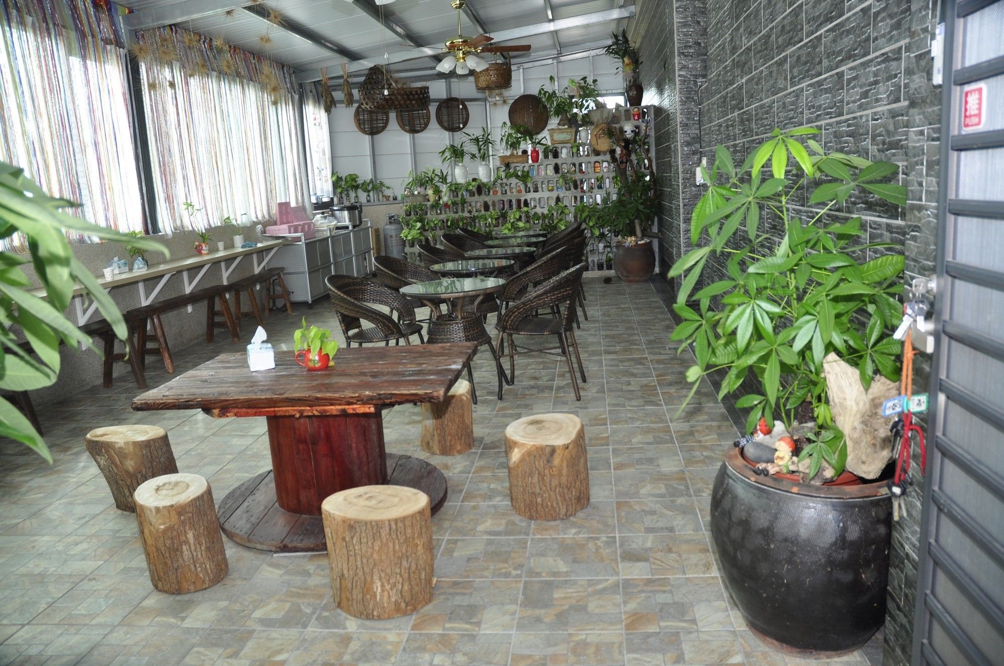 A restaurant with wooden tables and chairs, potted plants, and a stone-tiled floor.