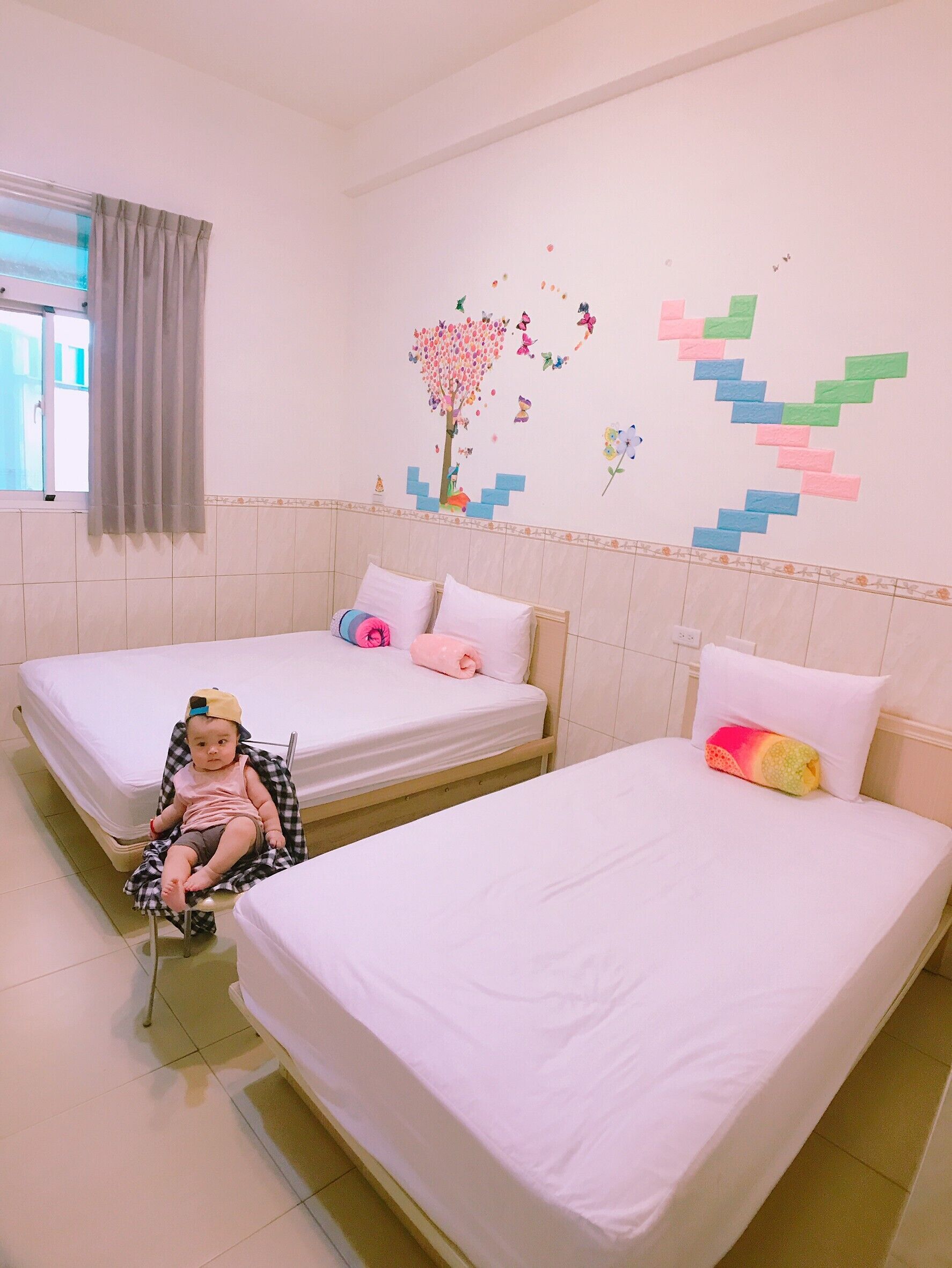 A hotel room with two beds, a window with curtains, and a wall decorated with colorful stickers.