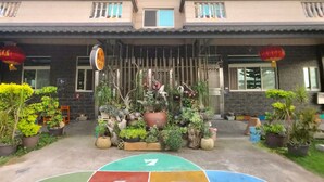 A multi-story building with a balcony on each floor, a small garden area with various plants, and a colorful hopscotch court in front. - tai-chia Bed and Breakfast (Jincheng)