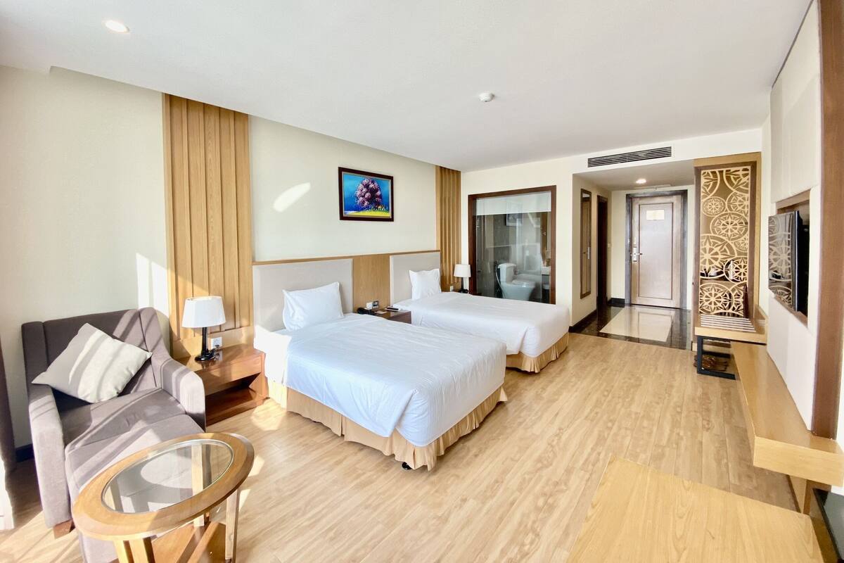 A hotel room with two beds, a sofa, a glass table, and a TV.