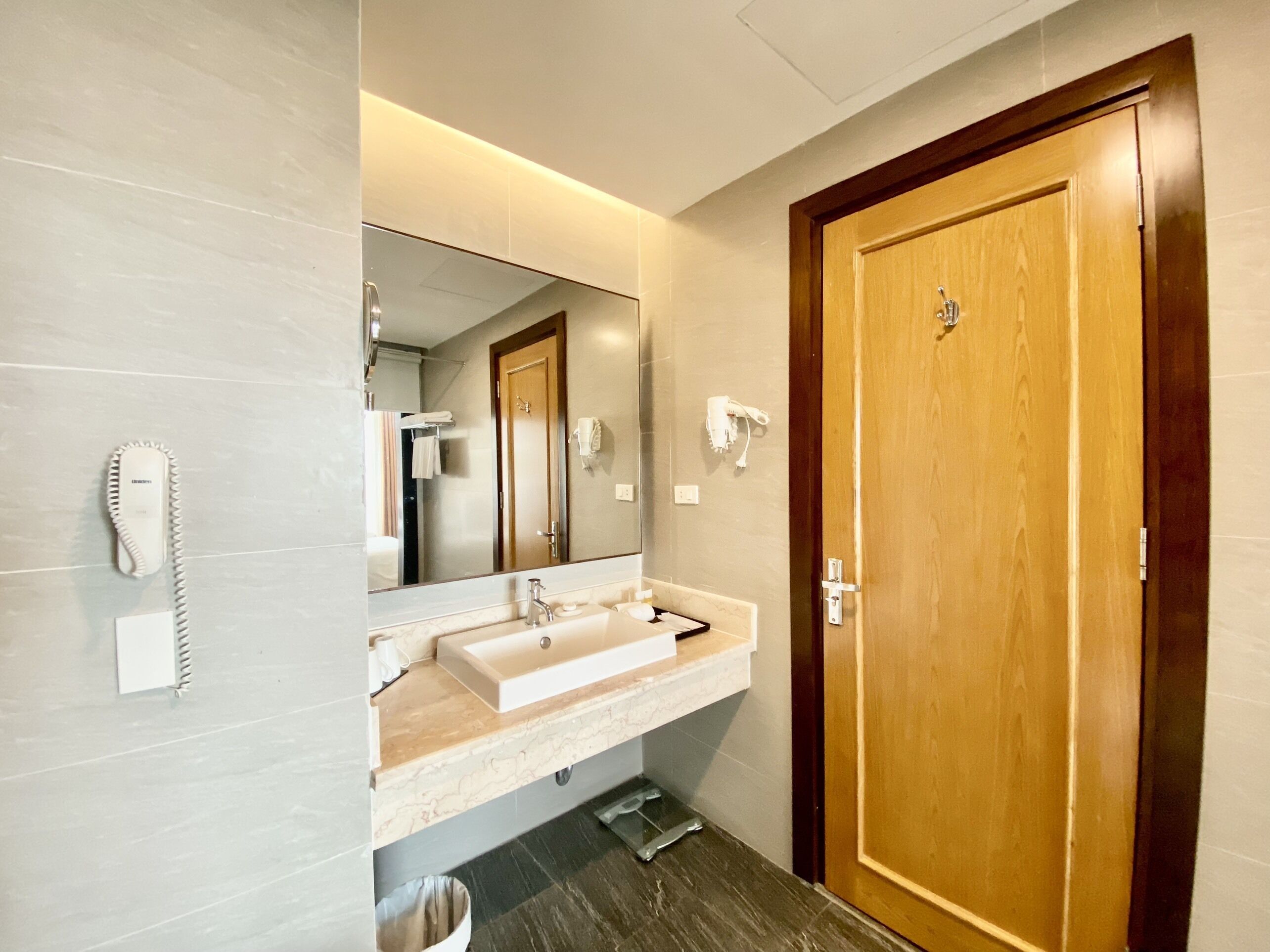 A modern bathroom with a large mirror, a sink, and a wooden door.