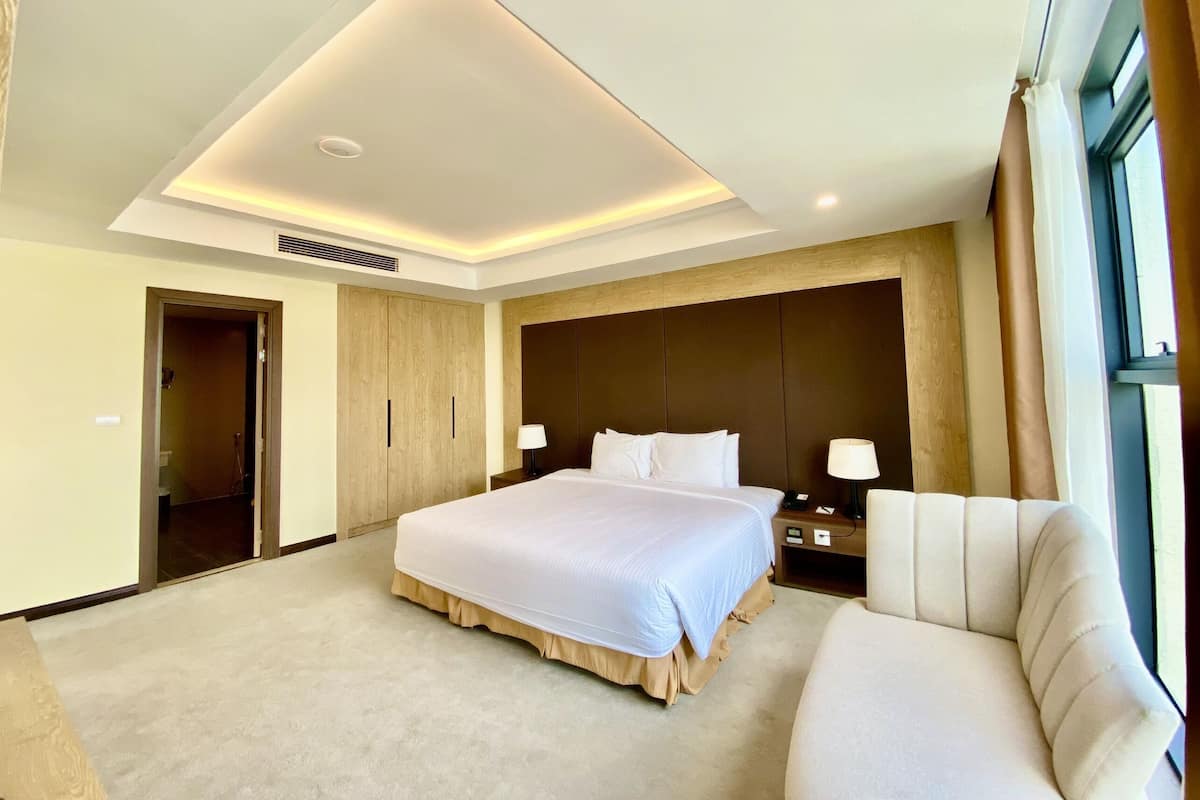 A modern hotel room with a large bed, a bedside table, a chair, and a large window.