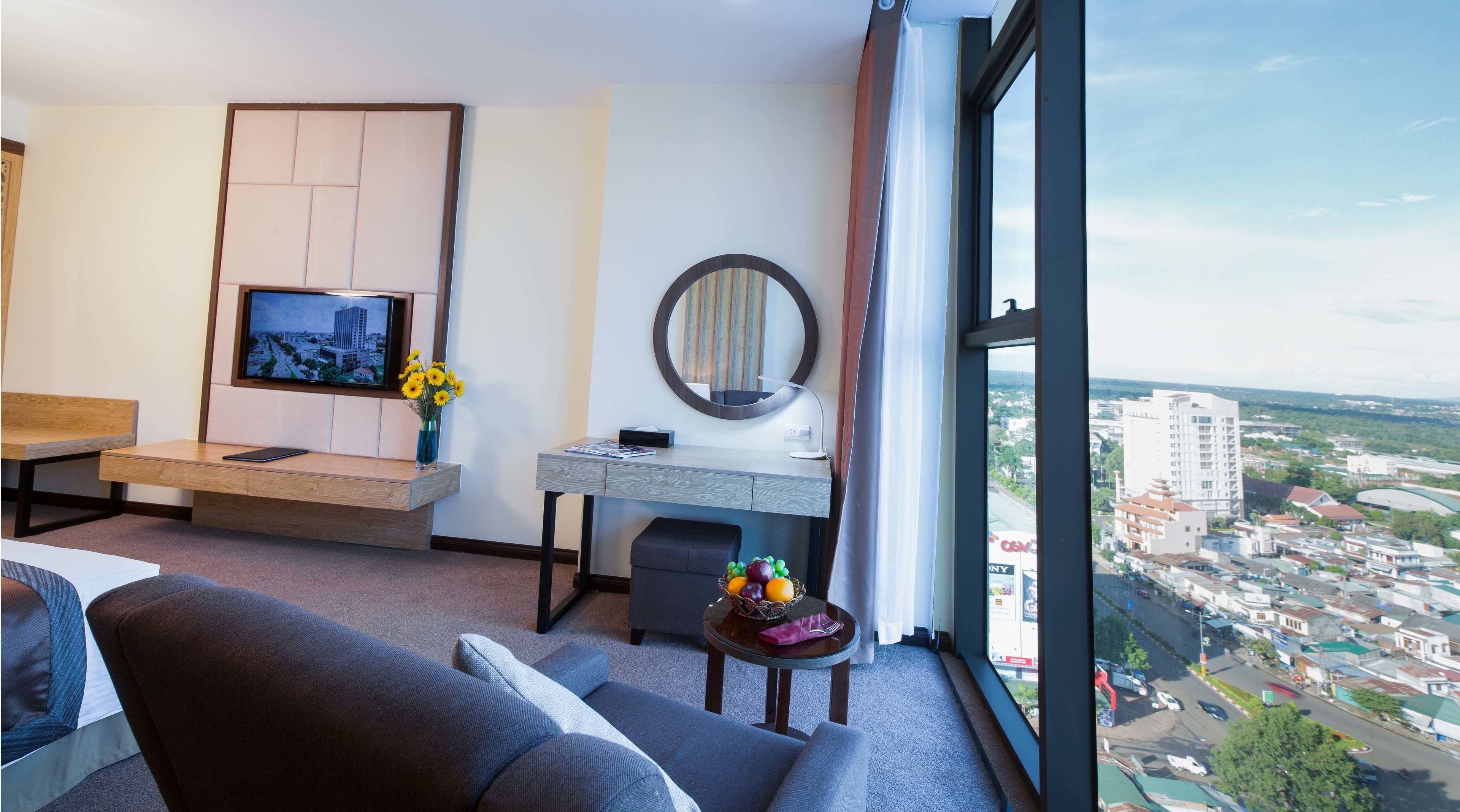 Een moderne hotelkamer met een groot raam, een bureau met een spiegel, een televisie en een bank.