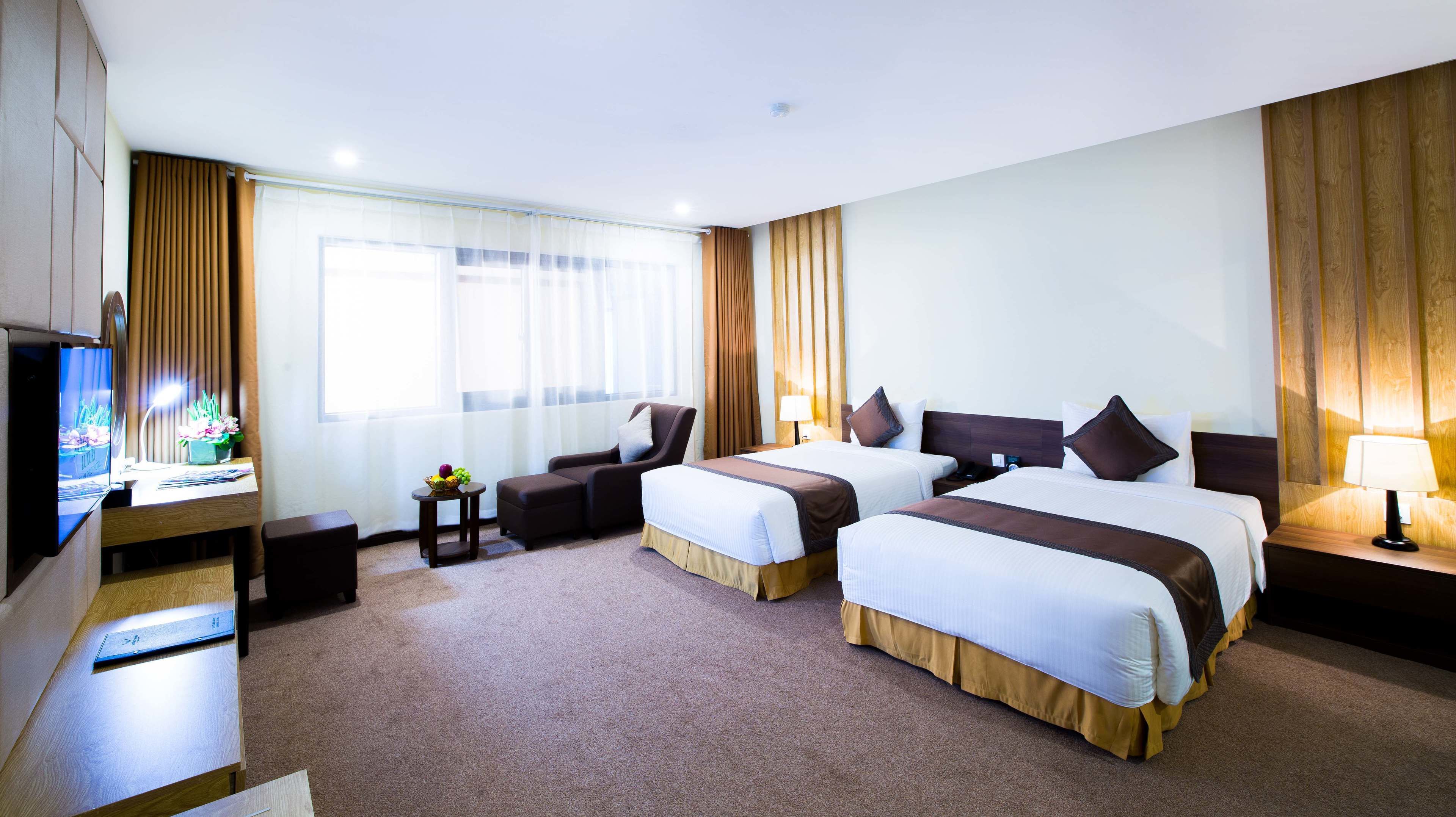 A hotel room with two beds, a desk with a computer, a TV, and a small table with a fruit bowl.