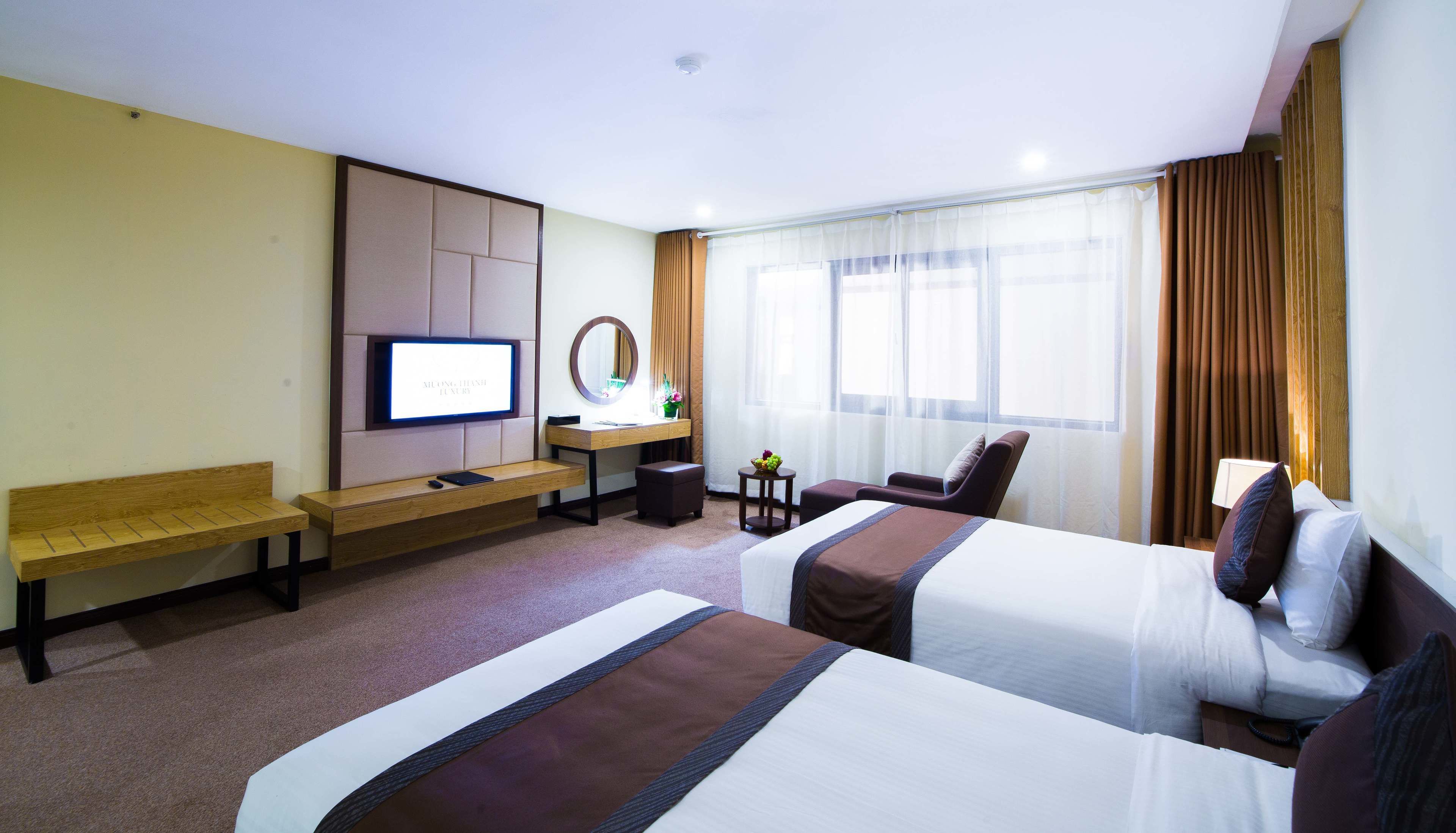 A hotel room with two beds, a desk with a computer, a TV, and a window with curtains.
