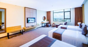 A hotel room with two beds, a TV, a bench, a small table with a mirror, and a view of the city. - Muong Thanh Luxury Buon Ma Thuot (Buon Ma Thuot)