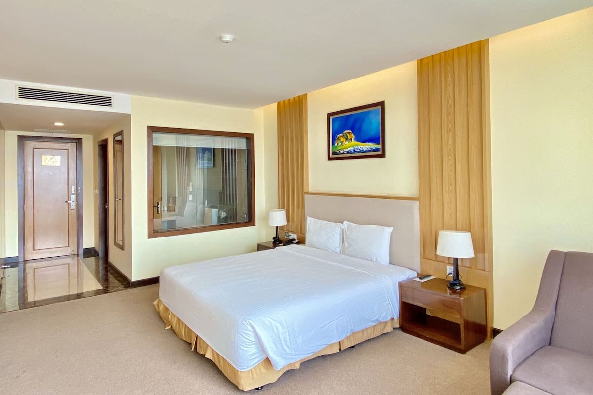 A hotel room with a large bed, bedside tables with lamps, a painting on the wall, and a door leading to another room.