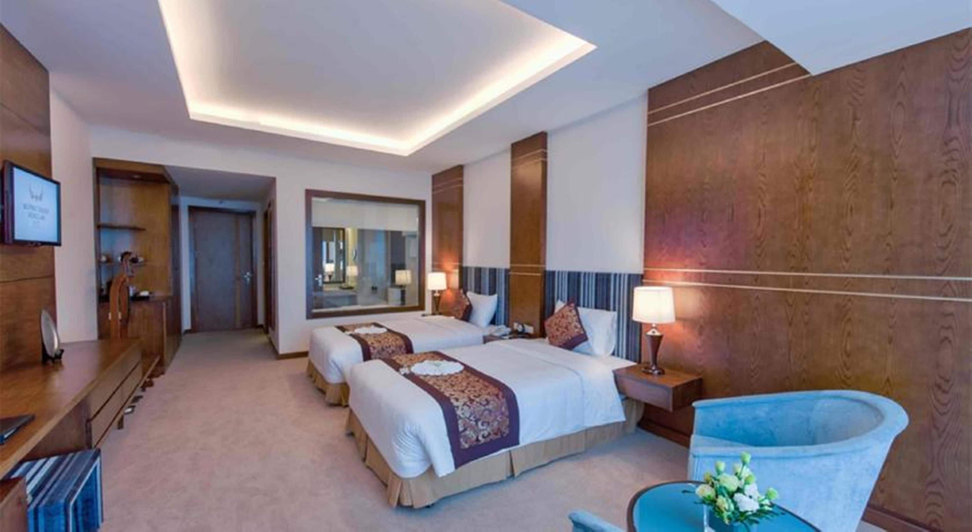 A hotel room with a large bed, bedside tables, a mirror, and a seating area with a chair and a small table.