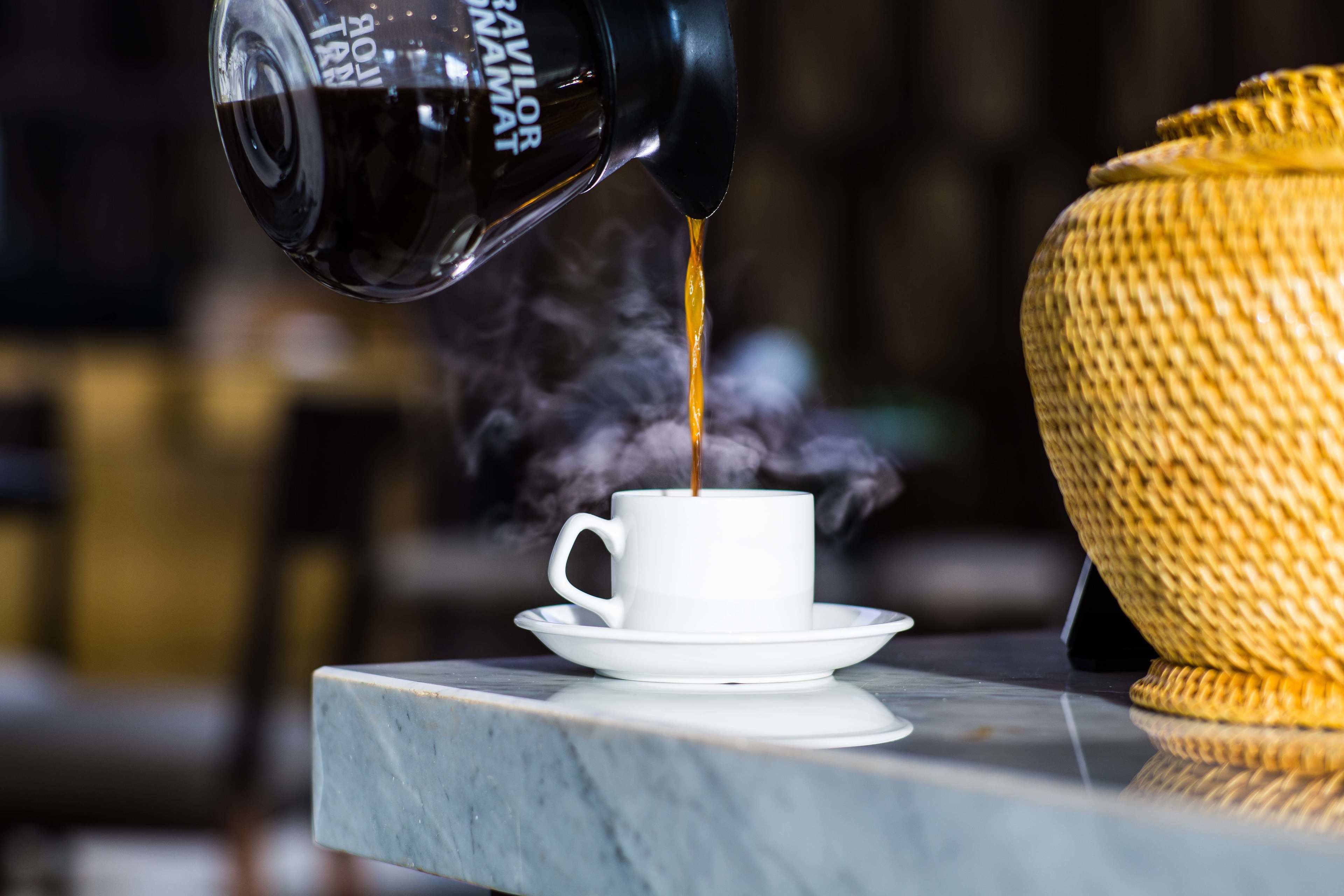 A coffee machine pouring coffee into a white cup on a marble table.